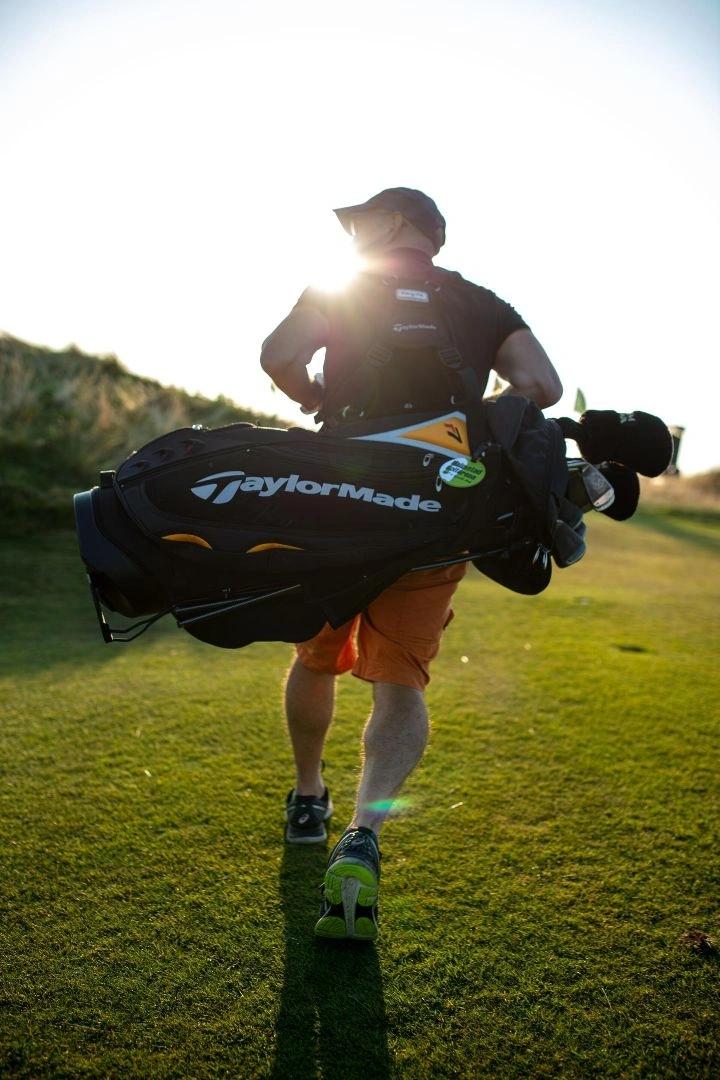 Golfeur portant son sac TaylorMade sur un parcours de résidence de luxe au coucher de soleil