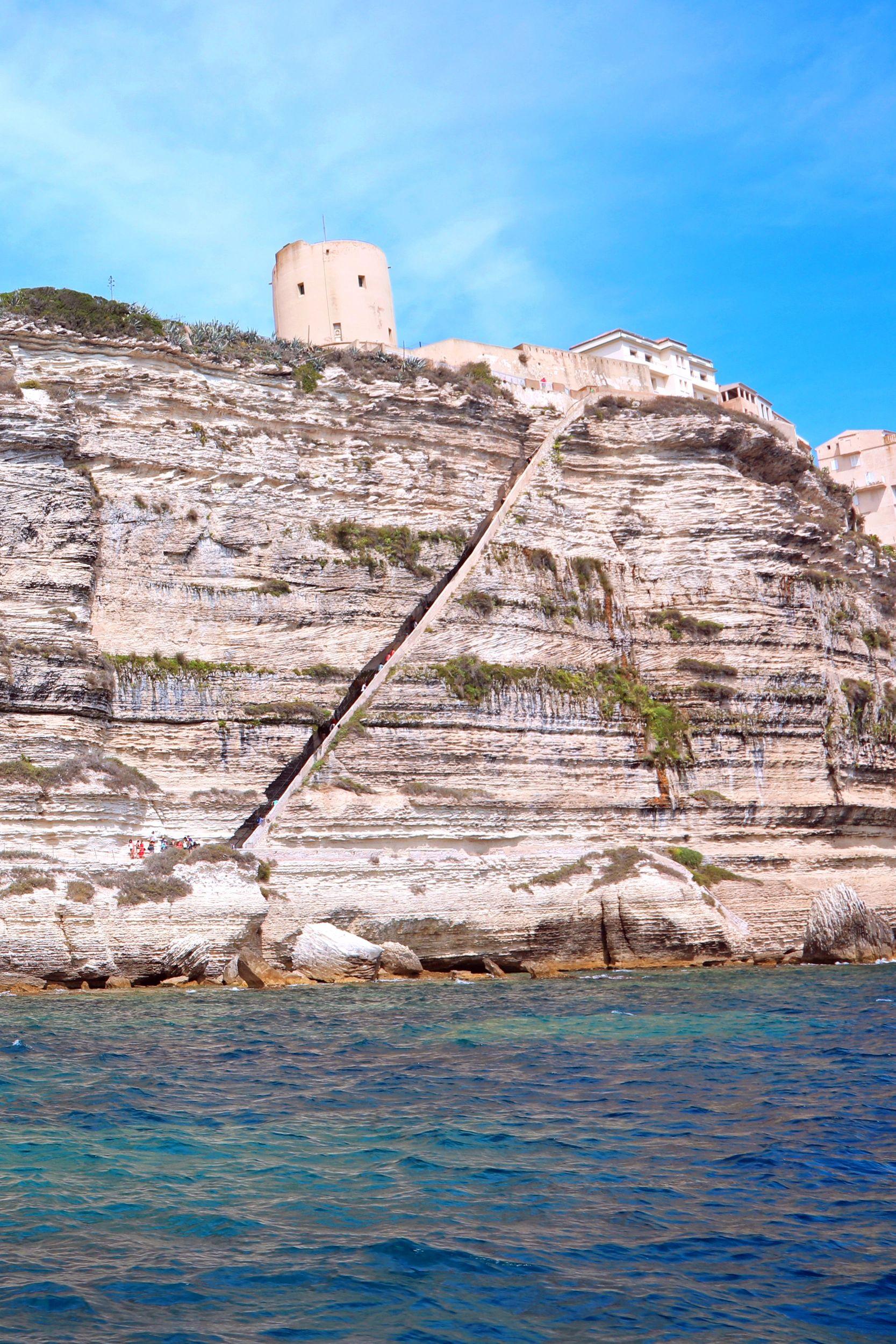 Vue côtière avec tour génoise sur falaise rocheuse et bateau en mer Méditerranée