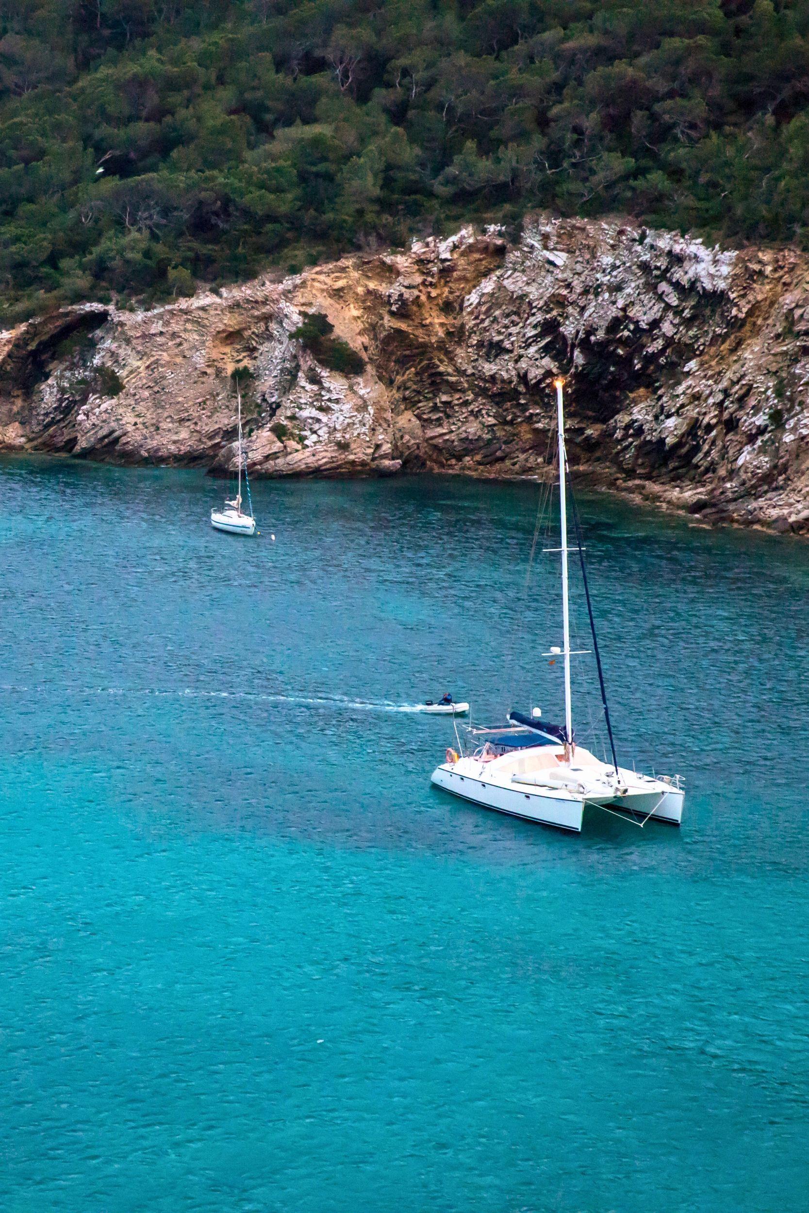 Bateau à voile ancré dans une crique méditerranéenne aux eaux turquoise et falaises rocheuses
