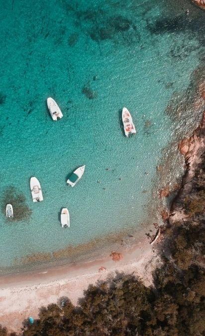 Vue aérienne de bateaux amarrés dans une eau turquoise près d'une résidence de luxe côtière