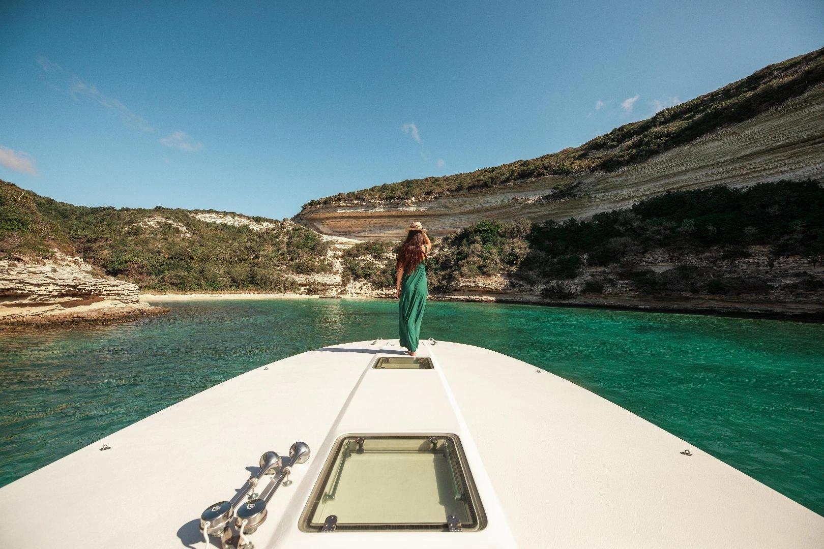 Femme sur un bateau de luxe naviguant près des falaises de Bonifacio en Corse avec eau turquoise