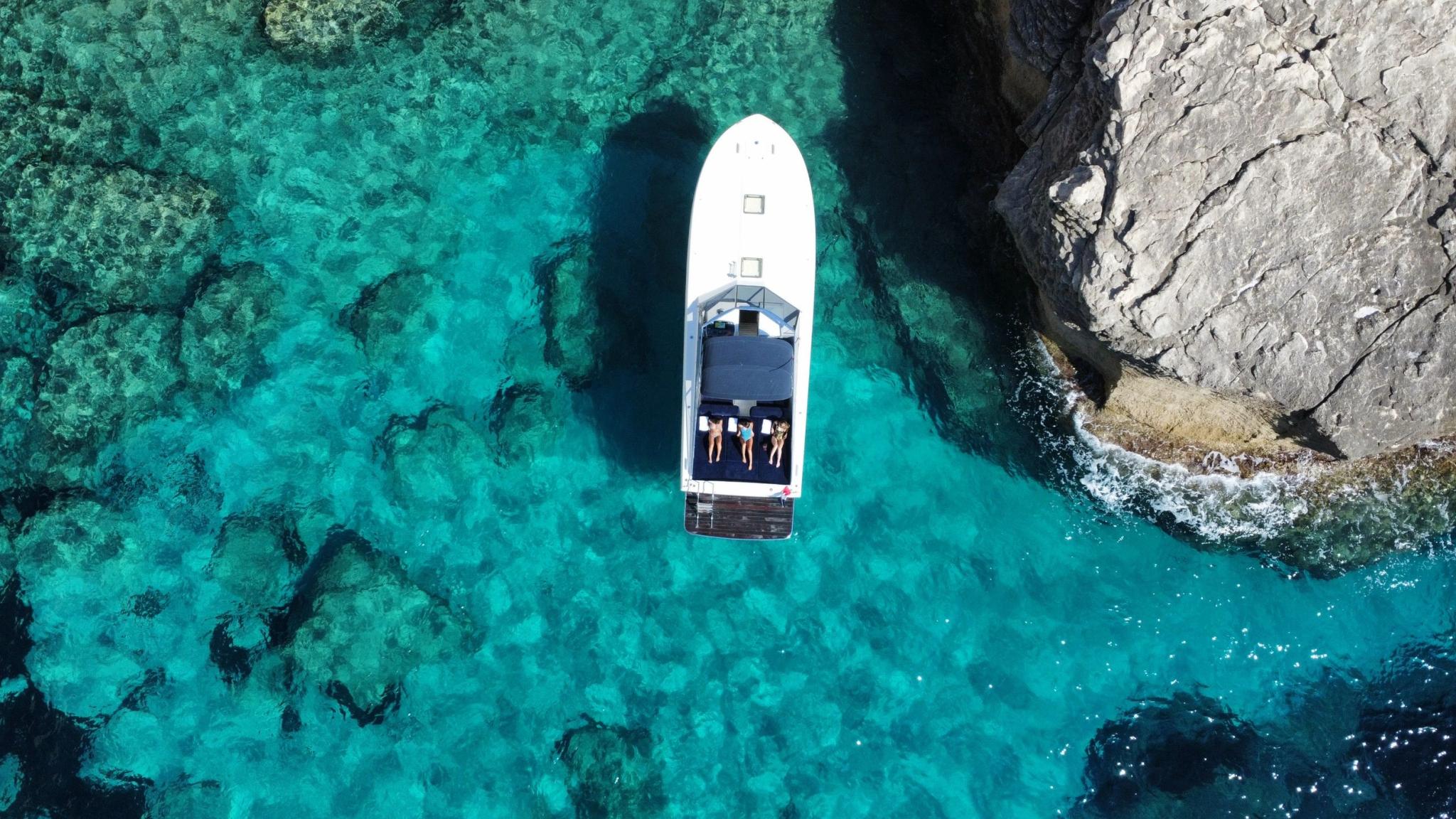 Bateau blanc amarré dans une crique avec eaux turquoise cristallines et rochers