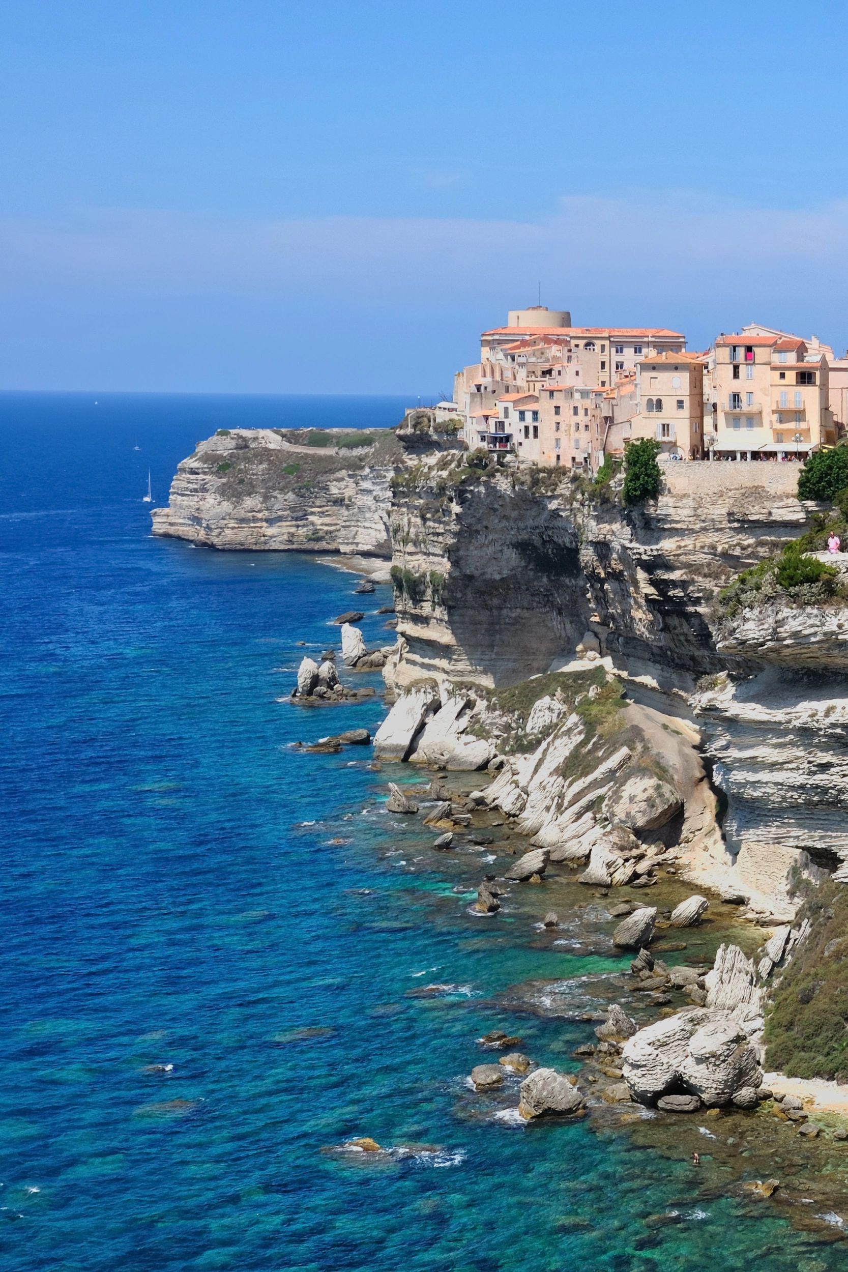 Vue panoramique de Bonifacio en Corse avec ses maisons perchées sur les falaises blanches et un bateau voilier en mer