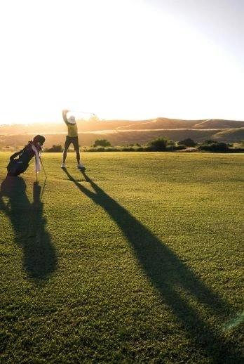 Deux personnes jouent au golf au coucher de soleil dans une résidence de luxe avec vue sur les montagnes