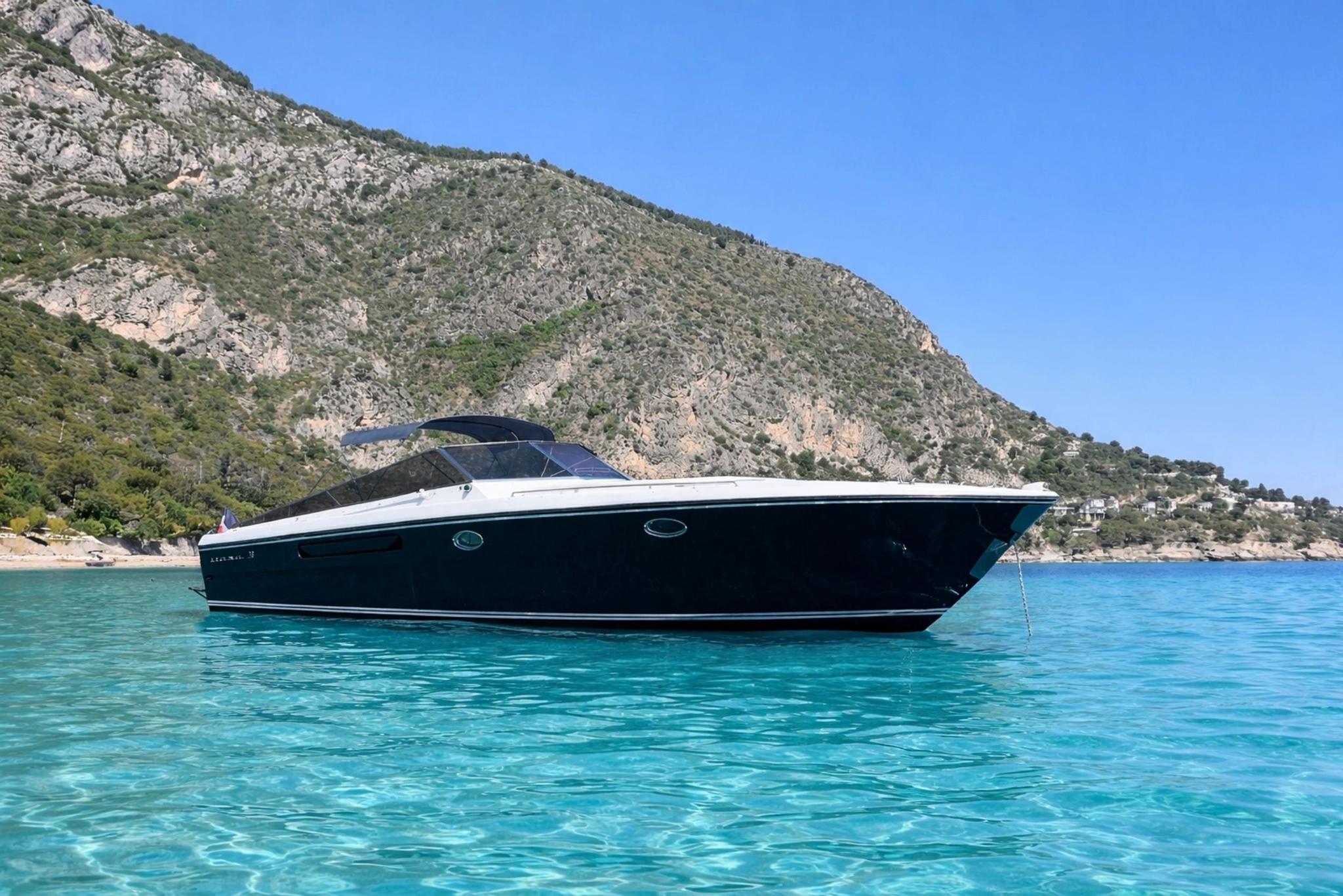 Bateau de luxe noir et blanc mouillé en eaux turquoise face aux falaises méditerranéennes