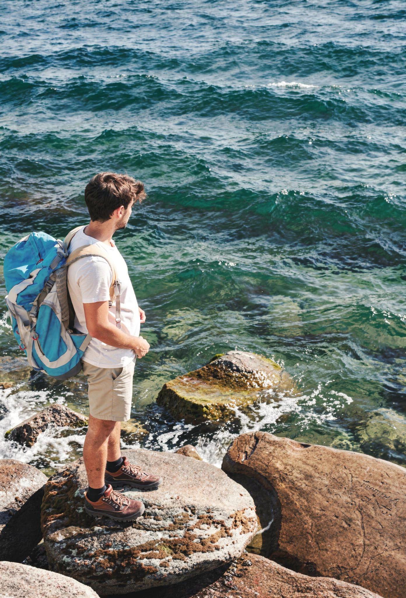 Randonneur avec sac à dos observant la mer turquoise depuis les rochers de Bonifacio